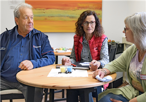Drei Mitarbeitende (von den Maltesern, Arbeiterwohlfahrt und Caritas) sitzen zusammen an einem Tisch im Hilfszentrum Schleidener Tal und tauschen sich aus.