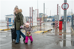 Eine junge, ukrainische Frau mit einem kleinen Mädchen halten sich an den Händen und überqueren die ukrainisch-rumänische Grenze