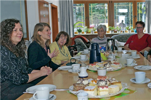 Zwei NRW-Landtagsabgeordnete der Grünen sitzen an einer gedeckten Kaffeetafel mit Bewohnerinnnen und Mitarbeitenden einer Einrichtung der Caritas Witten zusammen
