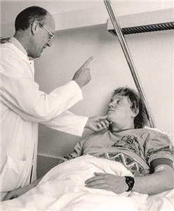 Ein Arzt steht vor einem im Krankenbett liegenden Patienten und führt eine Behandlung durch