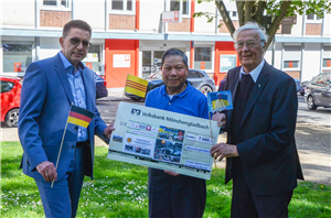 Van Ri Nguyen, Pfarrer Johannes van der Vorst und Frank Polixa stehen zusammen und halten Fähnchen von Deutschland, Südvietnam und der Ukraine hoch. Van Ri Nguyen trägt zudem einen großen Scheck.