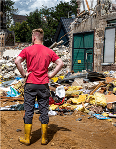 Ein Freiwilliger Helfer steht inmitten von durch die Flutkatastrophe 2021 zerstörten Gebäuden des Stadtteils Erftstadt-Blessem vor einem großen Müll- und Schutthaufen