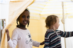 Ein Mädchen und ein Junge stehen in einer Kita unter einem selbstgebauten Zelt