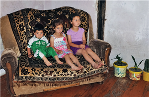 Drei armenische Kinder sitzen auf einem alten Sofa zusammen. Daneben stehen drei Blumentöpfe.