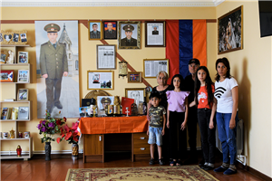 Eine sechsköpfige, armenische Familie steht in einem Wohnraum vor einer Wand, die zum Gedenken an verstorbene Verwandte mit Fotos und Erinnerungsstücken geschmückt ist