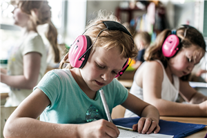 Zwei Mädchen mit einem rosafarbenden Gehörschutz, die ihre Hausaufgaben in einer OGS machen