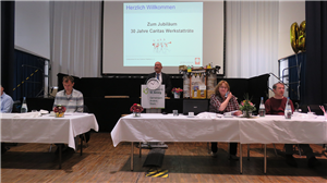 Der Paderborner Diözesan-Caritasdirektor Josef Lüttig steht beim 30-jährigen Jubiläum der Caritas-Werkstatträte vor einem Rednerpult und hält eine Rede. Im Vordergrund sitzen einige Teilnehmende.