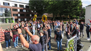 Die Teilnehmenden des 30-jährigen Jubiläums der Caritas-Werkstatträte, die auf einem Außengelände eine rote Schnur und einen goldenen Luftballon (Zahl 30) hochhalten