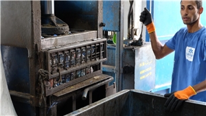 Ein Arbeiter bedient eine Plastikpresse, die transparente Flaschen presst. 