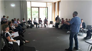 Oliver Kepka steht auf dem Barcamp 'Soziale Arbeit' 2017 in einem Tagungsraum innerhalb eines Stuhlkreises, in dem die Teilnehmer sitzen, und hält einen Vortrag