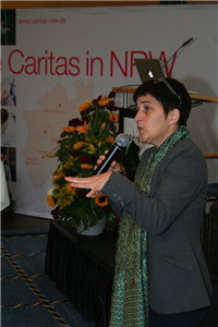 Ministerin Barbara Steffens steht mit einem Mikrofon neben einer Bühne mit Rednerpult und hält eine Rede