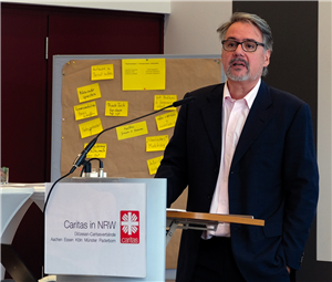 Dr. Frank Bauer steht bei der CiNW-Fachtagung 'Sozialer Arbeitsmarkt in Nordrhein-Westfalen' am 10.10.2019 an einem Pult und hält seinen Vortrag. Im Hintergrund steht eine Pinnwand mit gelben Zetteln.