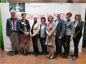 Die acht Referenten/-innen der Informationsveranstaltung zum neuen Pflegeberufegesetz in Dortmund stehen vor einem Faltdisplay der Caritas in NRW 