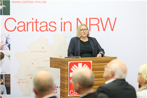 Essens Diözesan-Caritasdirektorin Sabine Depew steht beim Ruhrgebietstag vor einem Rednerpult und hält ihre Begrüßungsrede. Neben ihr ist ein Faltdisplay der Caritas in NRW zu sehen.