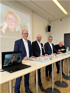 Die Referierende bei der CiNW-Fachtagung 'Soziale Betriebe stärken – Teilhabe nachhaltig gestalten' in Düsseldorf, die an einem langen Stehtisch stehen. Eine Referentin ist per Video zugeschaltet.