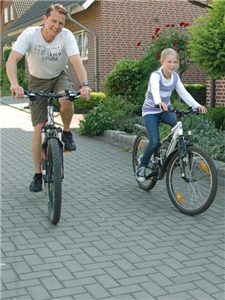 Ein Vater und seine Tochter fahren mit ihren Fahrrädern vor einem Wohnhaus 