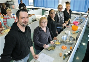 Ein Teilnehmer und vier Teilnehmerinnen stehen an einer Küchenzeile und bereiten Speisen zu.