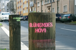 Zwei am Straßenrand platzierte Holzpfosten mit dem farbigen Schriftzug 