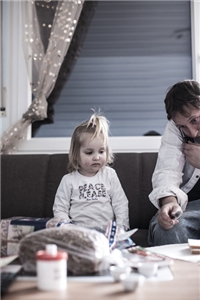 Ein Mädchen sitzt neben ihrem telefonierenden Vater auf einem Sofa vor einem gefüllten Wohnzimmertisch