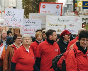 Die Teilnehmer einer Pflegedemonstration stehen mit Schildern auf einer Straße