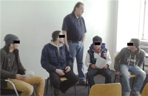 Vier Teilnehmer des Kurses sitzen nebeneinander auf Stühlen. Der Anti-Aggressivitäts-Trainer Hanjost Völker steht dahinter und redet mit einem der Teilnehmer.