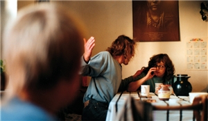 Gestellte Szene: Ein Mann sitzt mit einer Frau am Frühstückstisch. Der Mann beugt sich nach vorne und hebt bedrohlich seine rechte Hand, die Frau weicht zurück. Abseits beobachtet ein Junge die Szene.