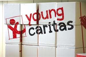 Eine Wand aus mit weißem Stoff bezogenen Sitzwürfeln. Diese wurden an meheren Seiten bedruckt und ergeben zusammengestellt das Logo der youngcaritas.