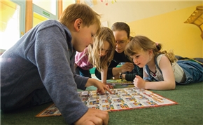 Ein Junge und zwei Mädchen spielen mit einer Betreuerin auf dem Fußboden.