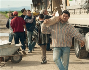 Eine Gruppe von Männern laden Fracht von einem LKW ab. Ein Mann kommt lächelnd dem Fotografen mit einem Zementsack entgegen.