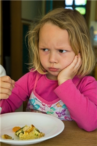 Ein Mädchen sitzt beim Mittagessen in einer trotzigen Pose vor ihrem halb gefüllten Teller