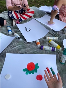 Kinderhände mit Farbe an den Fingern und Bilder auf einer Decke, die mit den Fingerfarben gemalt werden.