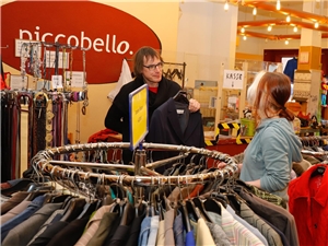 Eine Helferin zeigt einem Kunden im Caritas-Laden PiccobellO gebrauchte Kleidung.
