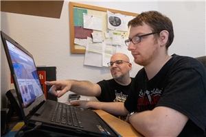 Ein Mann zeigt einem jungen Mann etwas an einem Laptop.