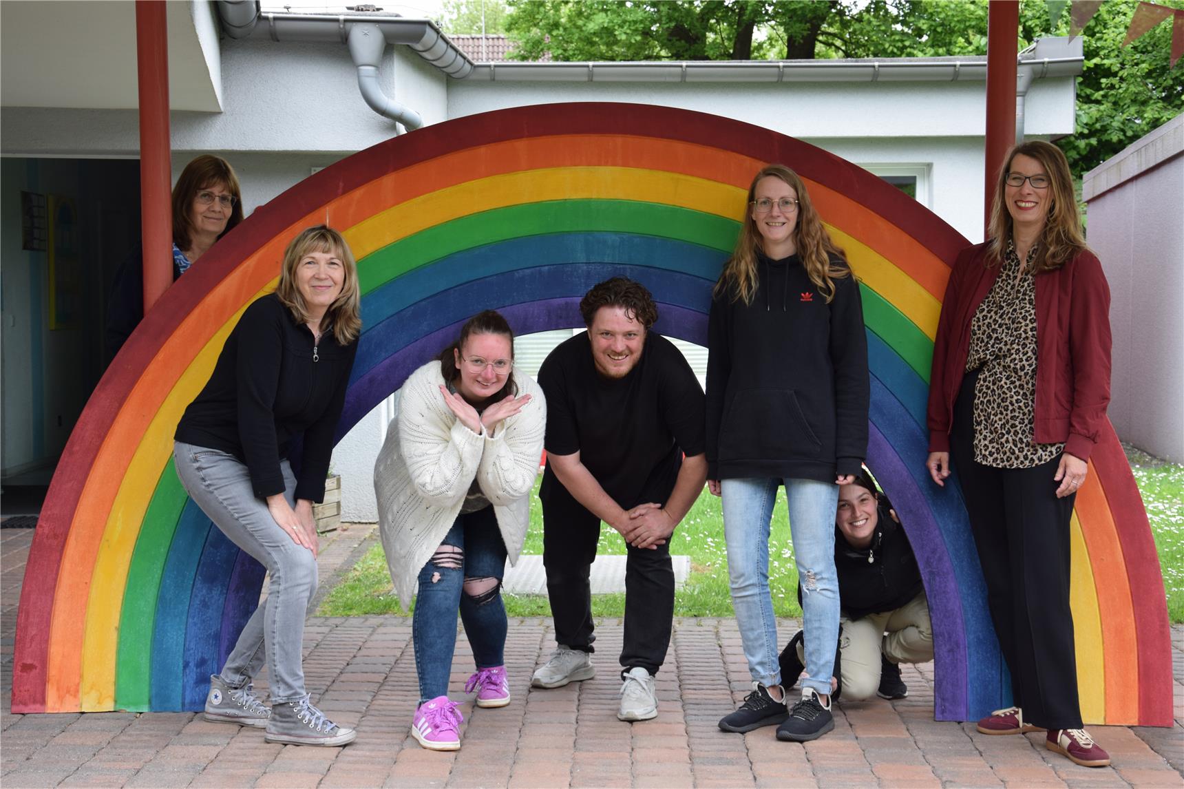 MItarbeitende der Kita Waisenhausstraße stehen vor und hinter einem Holzregenbogen