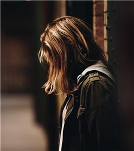Eine traurige Frau lehnt an eine Wand, ihr Gesicht ist hinter ihren Haaren verborgen.