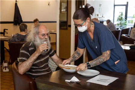 Ein alter Mann mit Bart bekommt im Gleis 51 der Caritas Oberhausen ein Mittagessen serviert.