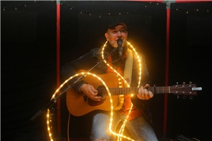 Musiker spielt im Dunkeln Gitarre und hat eine Lichtschlange um den Hals gelegt.