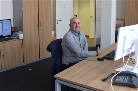 Ein Mann sitzt an einem Schreibtisch vor einem PC in einem Büro.