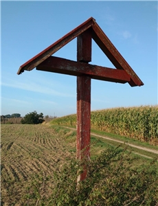Ein Holzkreuz auf einem Feld vor blauem Himmel.