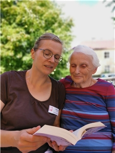 zwei Frauen sitzen auf einem Sofa, Frau liest älterer Frau aus einem Buch vor