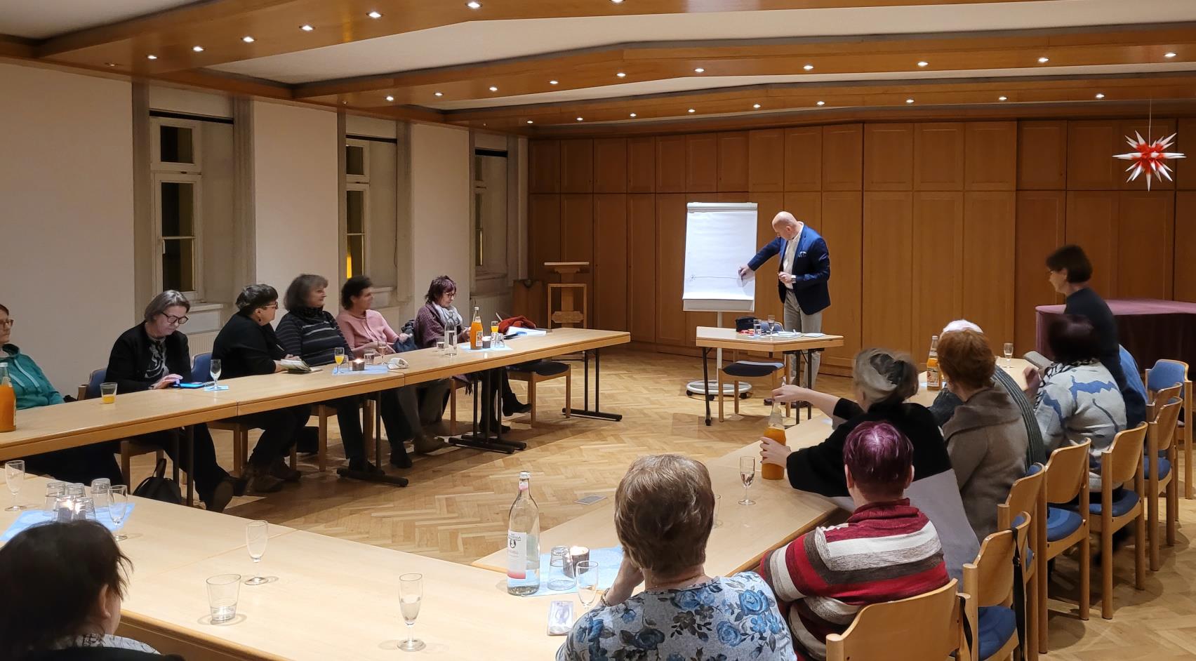 Menschen sitzen in einem Raum, in der Mitte ein Vortragender