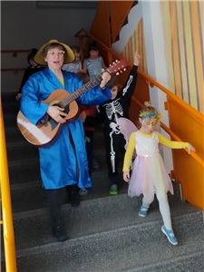 Eine Frau läuft singend mit Gitarre und Kindern durch ein Treppenhaus