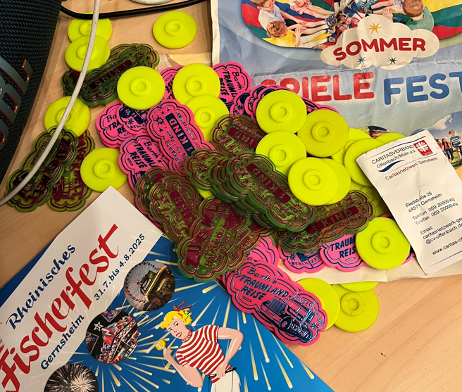Bunte Collage, auf der je ein Plakat zum Sommer-Spielefest und zum Fischerfest 2025 in Gernsheim zu sehen ist. Daneben verschiedenfarbige Fahr-Chips, die zur Mitfahrt auf verschiedenen Fahrgeschäften der Schausteller des Fischerfestes berechtigen.