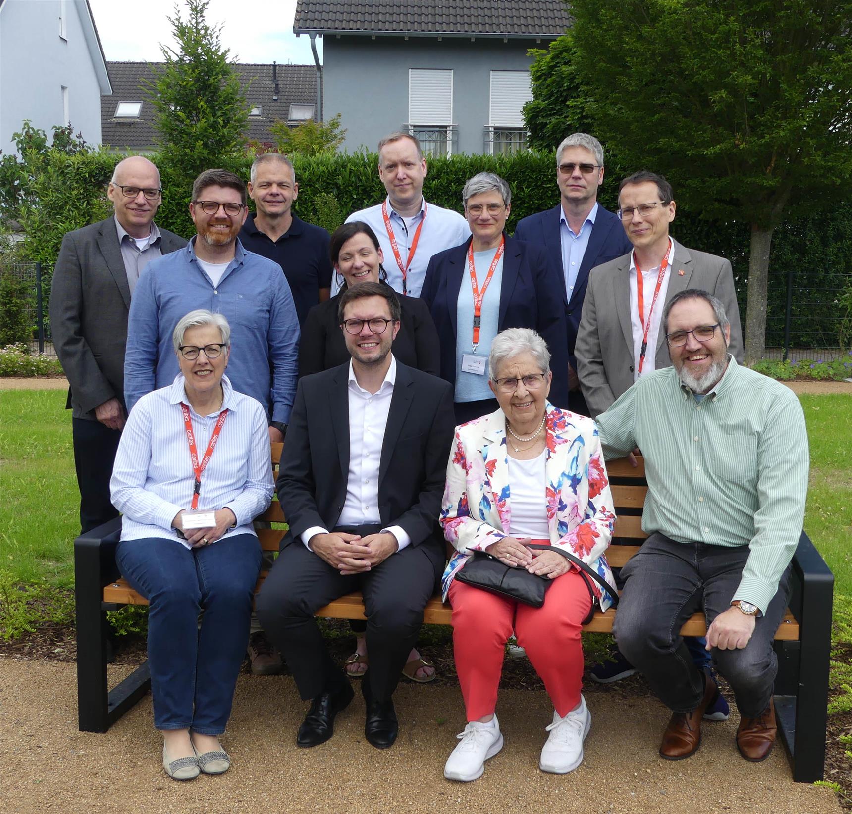 Gruppenbild mit Bürgermeister und Ortsvorsteher: vier Menschen sitzen auf einer Gartenbank - dahinter stehen weitere acht Frauen und Männer