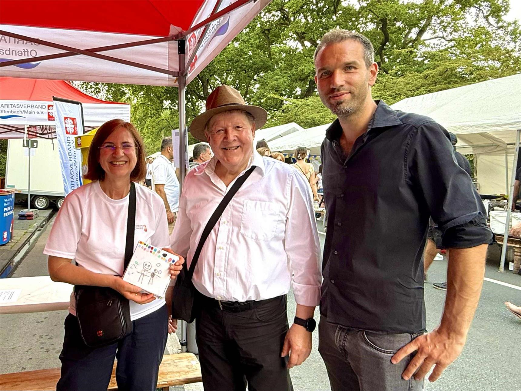 Sozialdezernent Martin Wilhelm und Stadtverordnetenvorsteher Stephan Färber schauen am Caritas-Infostand auf dem Mainuferfest vorbei. Caritas-Projektleiterin Edith Heilos informiert über aktuelle Angebote der Caritas in der Stadt.