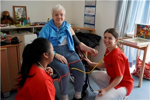 Zwei Pflegeschülerinnen messen einer Heimbewohnerin den Blutdruck