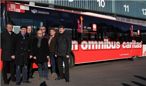 Eine Gruppe Menschen steht vor dem Bus der Stadtwerke mit der Aufschrift 'in omnibus caritas'