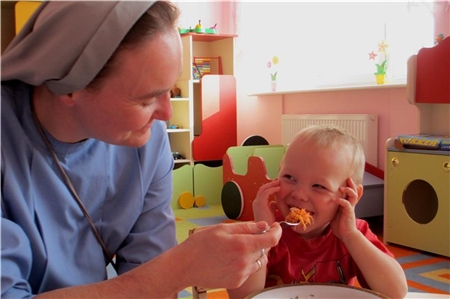 Ordensfrau hilft Kleinkind beim Essen