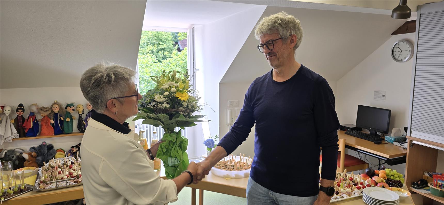 Ein Mann schüttelt einer älteren Frau in einem Raum die Hand.