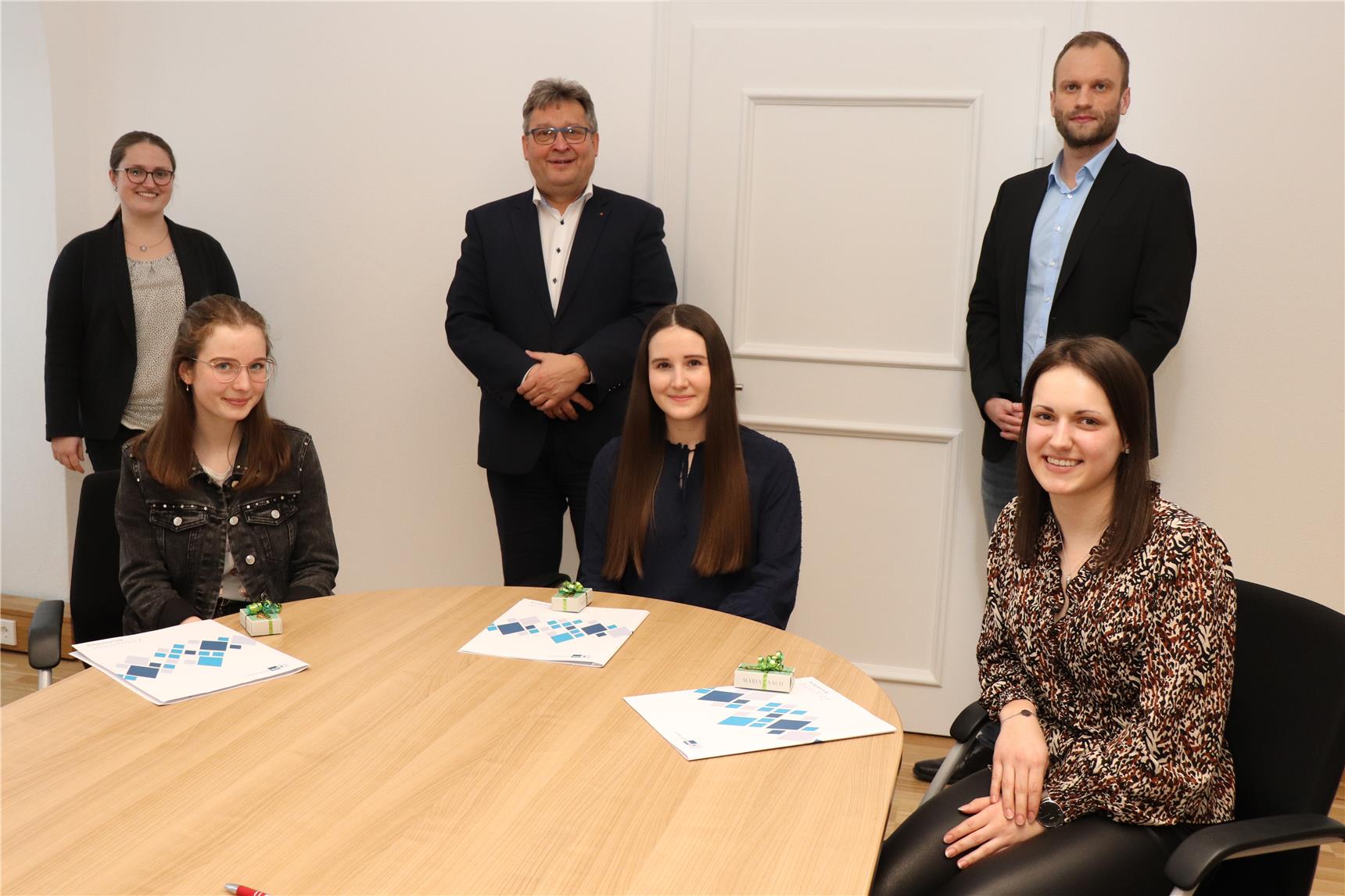 Drei junge Frauen sitzen auf einem Tisch, zwei Männer und eine Frau stehen dahinter.